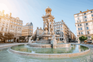 Fonte em praça europeia com esculturas e arquitetura clássica.