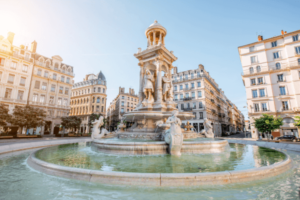 Fonte em praça europeia com esculturas e arquitetura clássica.