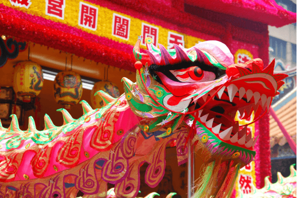 Dragão colorido em uma apresentação típica de festival chinês, com decoração vibrante ao fundo e lanternas tradicionais.